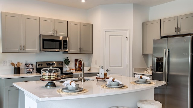 kitchen with gray cabinets, an island with sink, stainless steel appliances, and sink