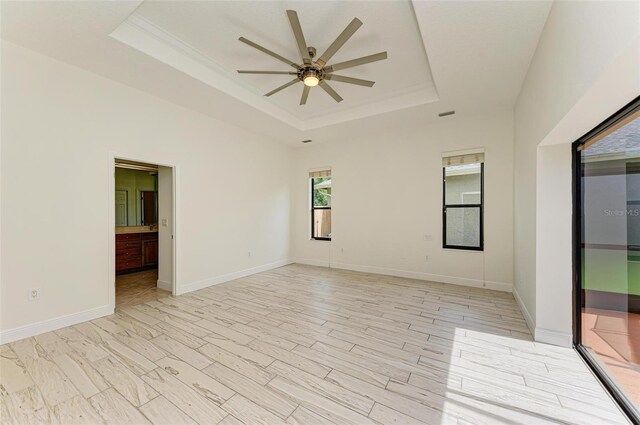 unfurnished room featuring ceiling fan, light wood-type flooring, and a tray ceiling