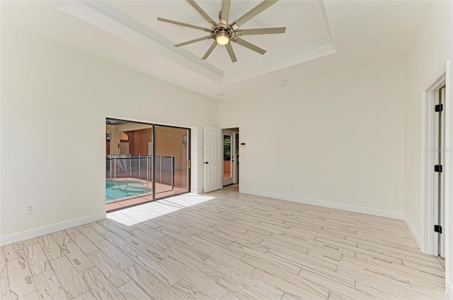 empty room with a raised ceiling, ceiling fan, and light wood-type flooring