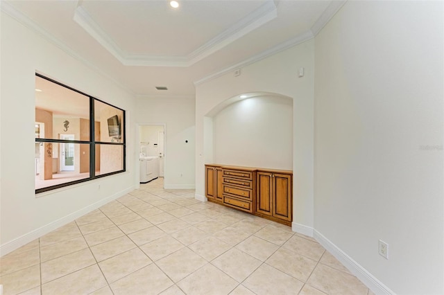 empty room with a raised ceiling, ornamental molding, light tile patterned floors, and separate washer and dryer