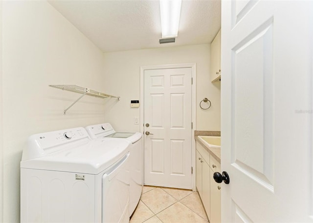 laundry area with a textured ceiling, light tile patterned flooring, separate washer and dryer, and cabinets