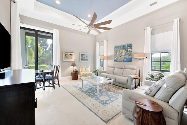 living room with ceiling fan, a wealth of natural light, and a raised ceiling