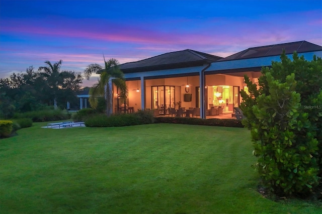 back house at dusk with a patio area and a lawn