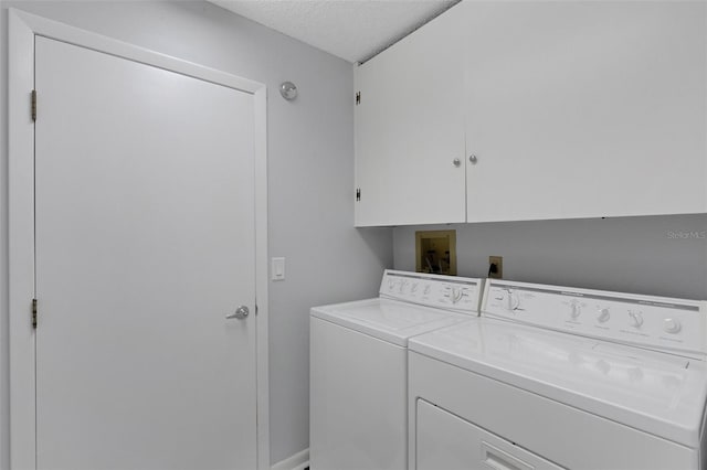 clothes washing area with washer and dryer, cabinets, and a textured ceiling