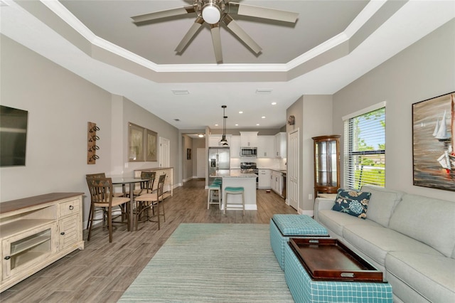 living room featuring a raised ceiling, ceiling fan, ornamental molding, and light hardwood / wood-style floors