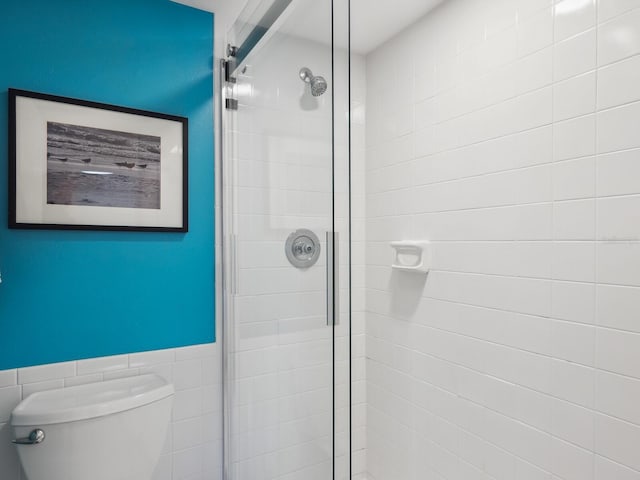 bathroom with tile walls, toilet, and a shower with shower door