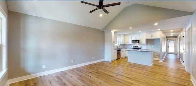 kitchen featuring tasteful backsplash, vaulted ceiling, a kitchen island, stainless steel appliances, and white cabinets