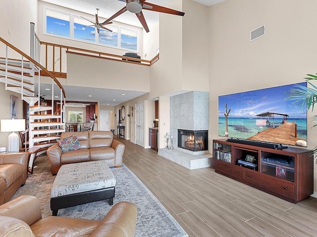 living room featuring ceiling fan, a towering ceiling, a fireplace, and light hardwood / wood-style flooring