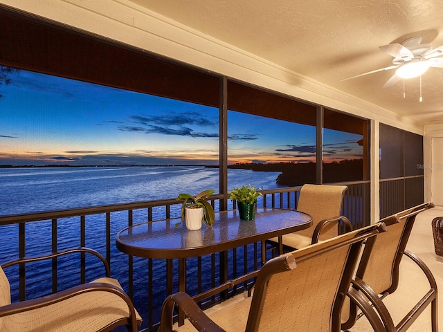 sunroom featuring ceiling fan and a water view