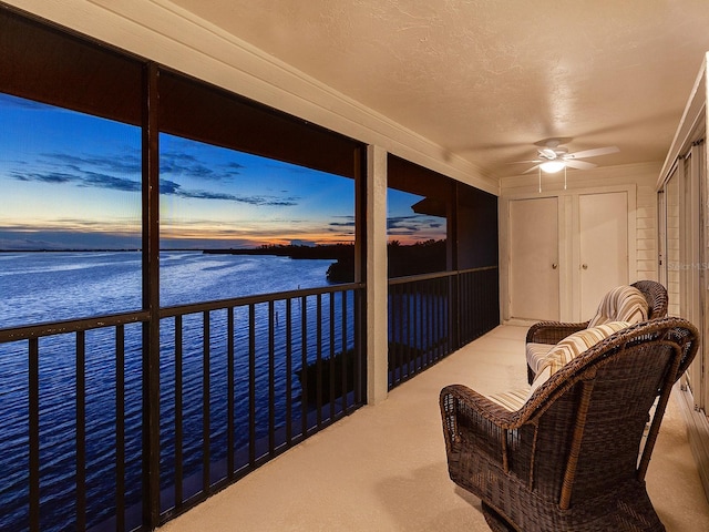 sunroom featuring ceiling fan and a water view