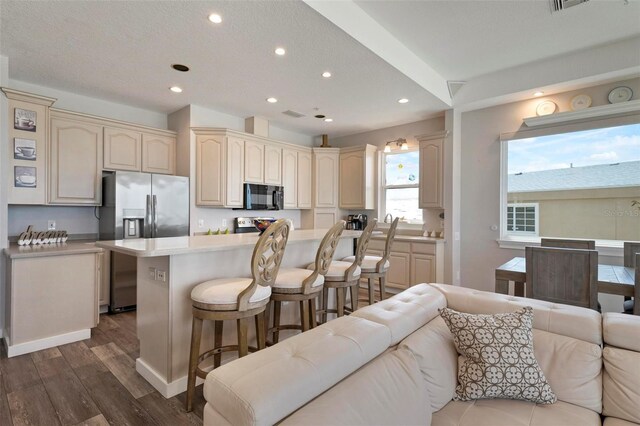 kitchen featuring a kitchen bar, cream cabinetry, open floor plan, and appliances with stainless steel finishes