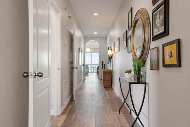 hallway featuring recessed lighting, light wood-style floors, arched walkways, and baseboards