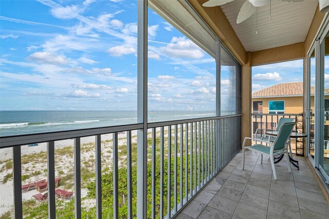 unfurnished sunroom with a beach view, a ceiling fan, and a water view