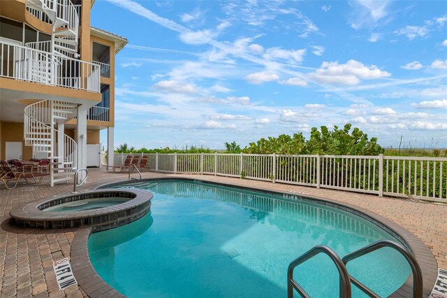 community pool with stairs, a patio area, fence, and a hot tub