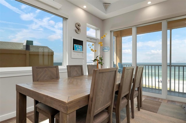 dining area with a water view, light wood-style flooring, recessed lighting, a view of the beach, and baseboards