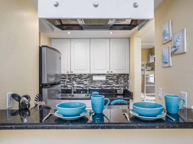 kitchen with kitchen peninsula, sink, tasteful backsplash, white cabinetry, and stainless steel refrigerator