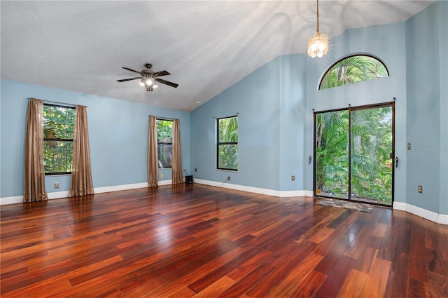 empty room with a textured ceiling, ceiling fan with notable chandelier, dark hardwood / wood-style floors, and high vaulted ceiling