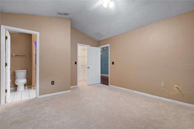 unfurnished bedroom featuring a textured ceiling, lofted ceiling, light colored carpet, ensuite bathroom, and a spacious closet