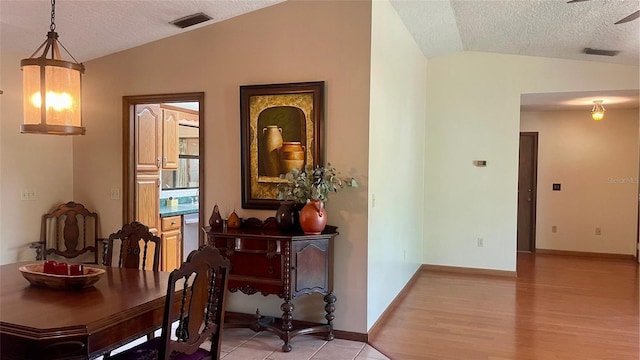 dining area with lofted ceiling, a textured ceiling, and light hardwood / wood-style flooring