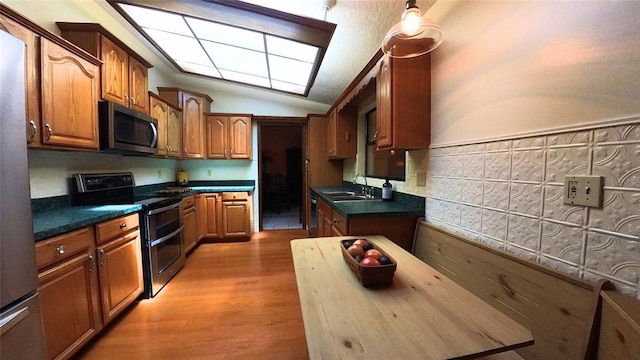 kitchen with stainless steel appliances, vaulted ceiling, sink, and light wood-type flooring