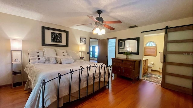 bedroom featuring dark hardwood / wood-style floors, connected bathroom, ceiling fan, a barn door, and a textured ceiling