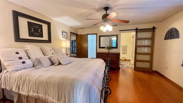 bedroom with ensuite bath, ceiling fan, wood-type flooring, a textured ceiling, and a barn door