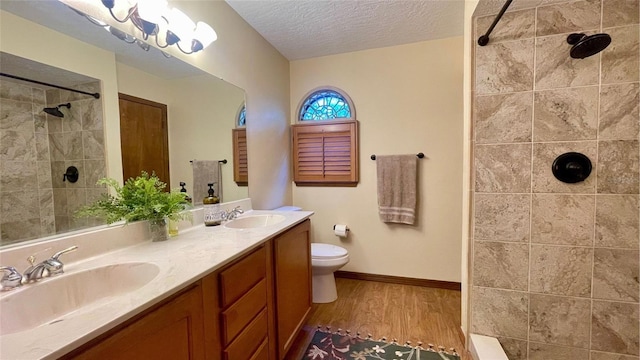 bathroom featuring vanity, a tile shower, wood-type flooring, a textured ceiling, and toilet