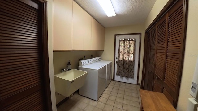 clothes washing area featuring cabinets, sink, washing machine and clothes dryer, and a textured ceiling