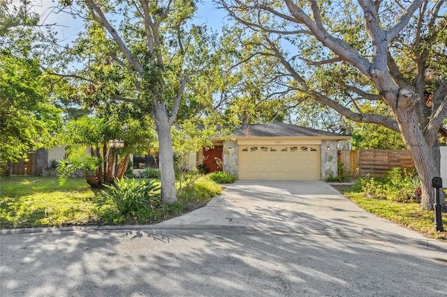 view of front of property with an attached garage, fence, stone siding, and driveway