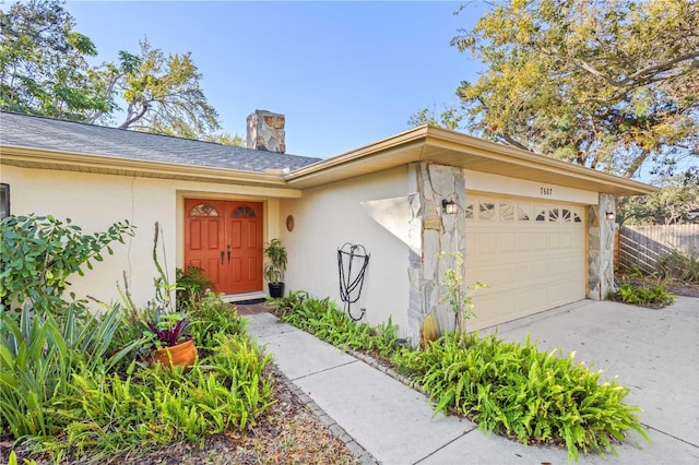 view of exterior entry featuring fence, driveway, a chimney, stucco siding, and a garage