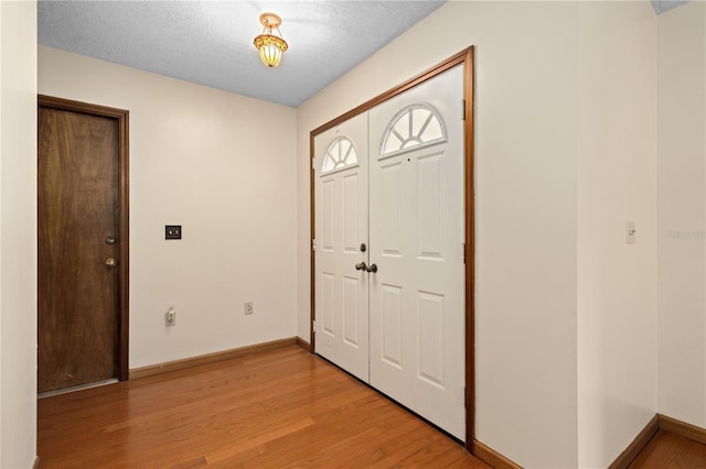 foyer entrance featuring baseboards, light wood-type flooring, and a textured ceiling