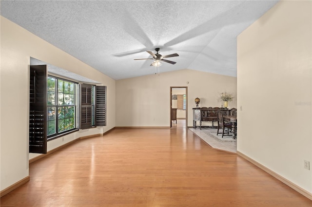 spare room with light wood-type flooring, a ceiling fan, a textured ceiling, baseboards, and vaulted ceiling