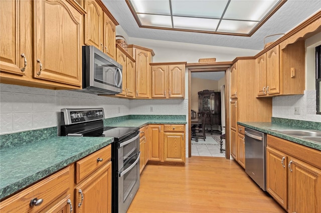 kitchen with a sink, backsplash, dark countertops, stainless steel appliances, and light wood finished floors