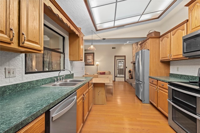 kitchen with dark countertops, appliances with stainless steel finishes, light wood-type flooring, and a sink