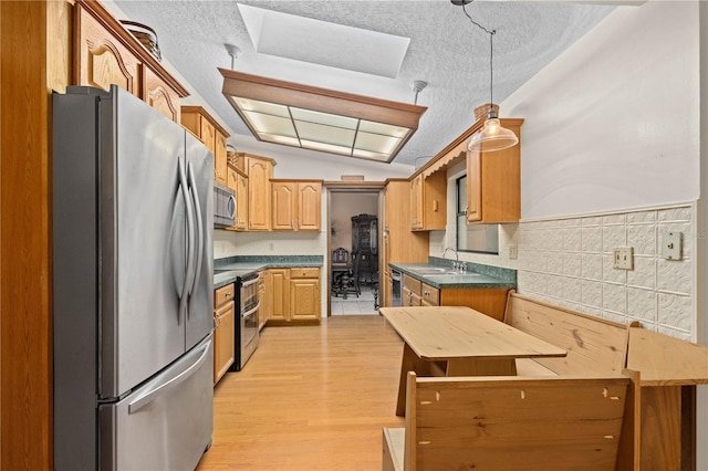 kitchen with dark countertops, vaulted ceiling, stainless steel appliances, light wood-style floors, and a textured ceiling