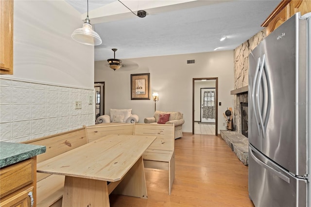 kitchen with visible vents, light wood-style flooring, decorative light fixtures, freestanding refrigerator, and a fireplace