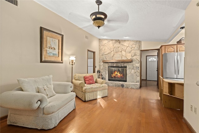 living area featuring visible vents, a ceiling fan, wood finished floors, a fireplace, and lofted ceiling