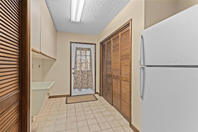 laundry room featuring light tile patterned floors, cabinet space, and a textured ceiling