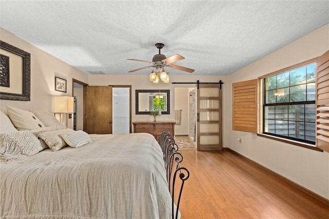 bedroom with wood finished floors, baseboards, ceiling fan, a textured ceiling, and a barn door