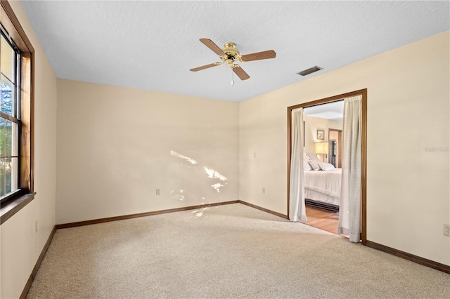 empty room with visible vents, light carpet, a textured ceiling, baseboards, and ceiling fan