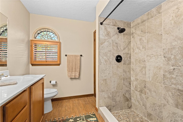 bathroom with baseboards, toilet, a tile shower, wood finished floors, and vanity