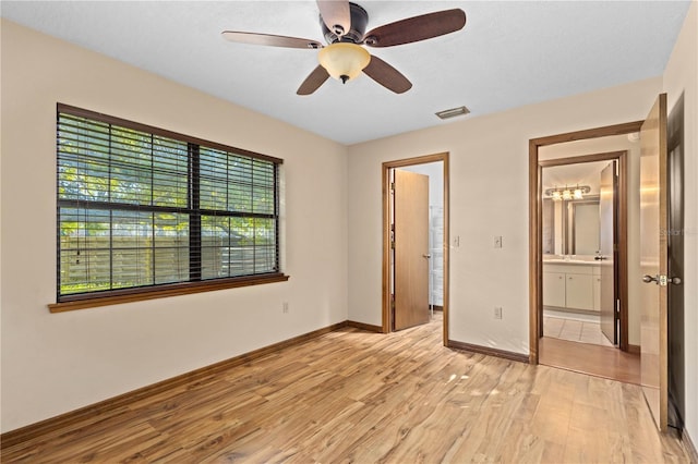 unfurnished bedroom featuring a ceiling fan, visible vents, baseboards, light wood-style floors, and ensuite bathroom