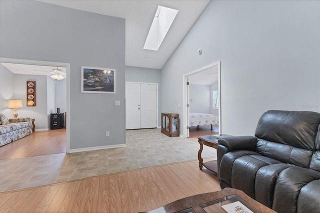 living room with light hardwood / wood-style floors, ceiling fan, a skylight, and high vaulted ceiling