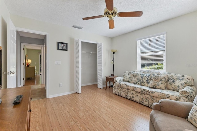 living room featuring ceiling fan, a textured ceiling, and light hardwood / wood-style floors