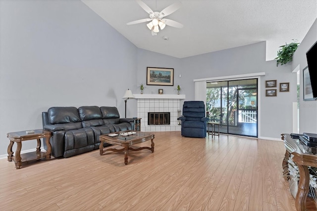 living room featuring ceiling fan, lofted ceiling, a textured ceiling, a fireplace, and light hardwood / wood-style floors