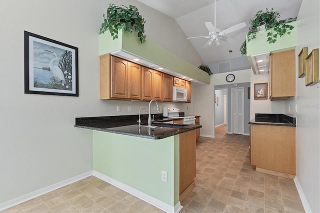 kitchen featuring ceiling fan, sink, kitchen peninsula, white appliances, and dark stone countertops