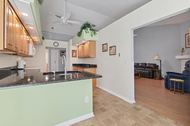 kitchen with kitchen peninsula, light wood-type flooring, ceiling fan, dark stone counters, and sink