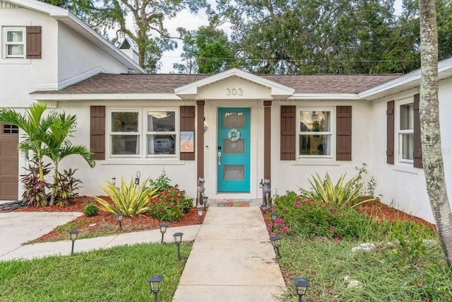 entrance to property with stucco siding, a shingled roof, and a garage