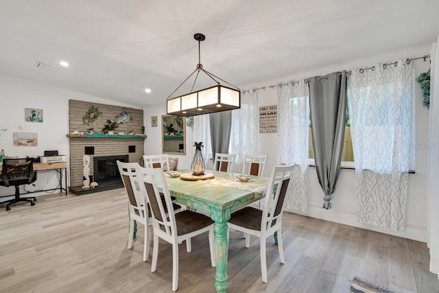 dining space with light wood-type flooring, lofted ceiling, and a brick fireplace