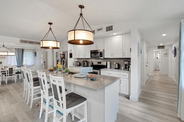 kitchen featuring an island with sink, decorative light fixtures, stainless steel appliances, and white cabinets